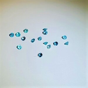 May include: Assortment of small, round, and triangular blue gemstones on a white surface.