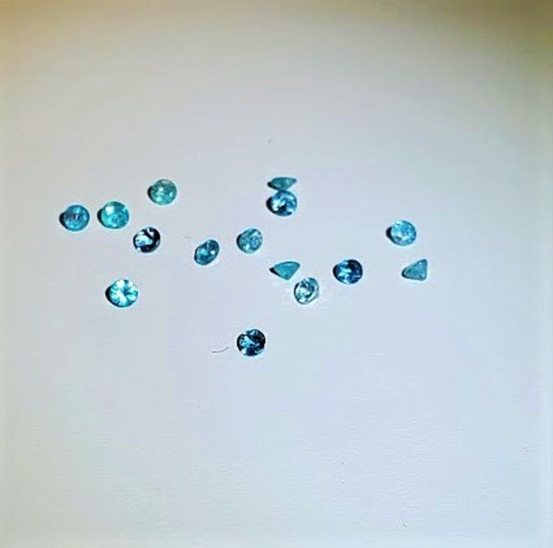 May include: Assortment of small, round, and triangular blue gemstones on a white surface.
