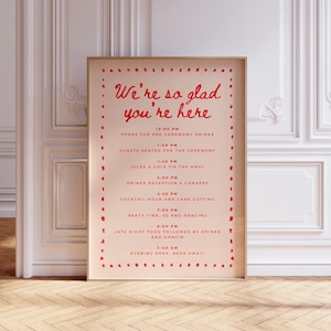Könnte beinhalten: Ein rechteckiges Hochzeitstafel-Schild mit hellrosa Hintergrund und roter Schrift. Das Schild hat einen roten, gepunkteten Rand und den Text: We're so glad you're here, gefolgt von einem Zeitplan der Veranstaltungen von 12:00 bis 3:00 Uhr morgens.
