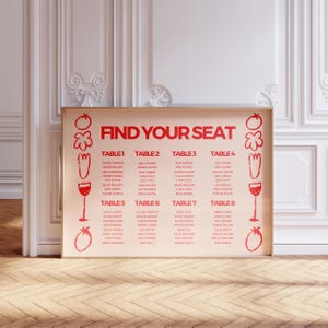Op de afbeelding: Een ingelijste trouwzittingstabel met de woorden "FIND YOUR SEAT" in het rood. De tabel bevat namen onder de tafelnummers 1-8. Rode illustraties van tomaten, wortelen en wijnglazen versieren de randen.
