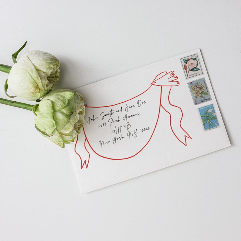 May include: A white envelope featuring a red line drawing of a bird carrying a banner. The address reads John Smith and Jane Doe, 5678 Park Avenue, Apt B, New York, NY 10065. Three postage stamps are affixed to the top right corner, and two pale green flowers are positioned to the left.
