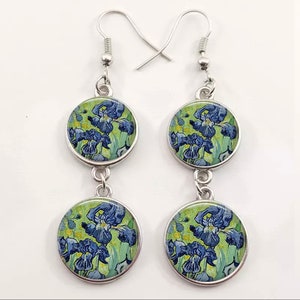 May include: A pair of silver dangle earrings with two round glass charms featuring a painting of blue irises on a green background.