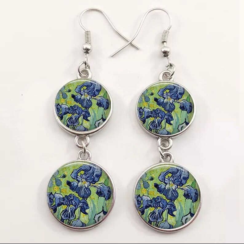 May include: A pair of silver dangle earrings with two round glass charms featuring a painting of blue irises on a green background.