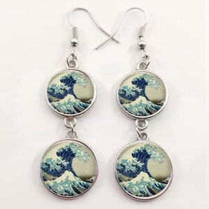 May include: A pair of silver dangle earrings with two round glass charms featuring a print of The Great Wave off Kanagawa by Katsushika Hokusai.