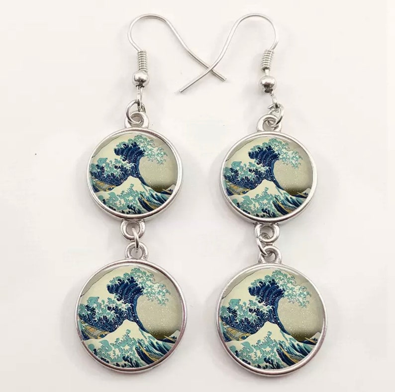 May include: A pair of silver dangle earrings with two round glass charms featuring a print of The Great Wave off Kanagawa by Katsushika Hokusai.