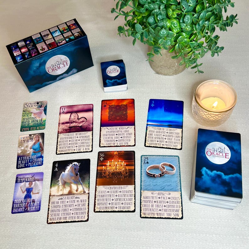 K&ouml;nnte beinhalten: Eine Auslage von Orakelkarten mit einer blau-wei&szlig;en Schachtel, einer Kerze und einem Stapel Karten mit dem Text "The In2it Oracle" auf der Vorderseite. Die Karten zeigen Bilder eines Herzens, eines Pferdes, eines Kronleuchters und zweier Ringe.