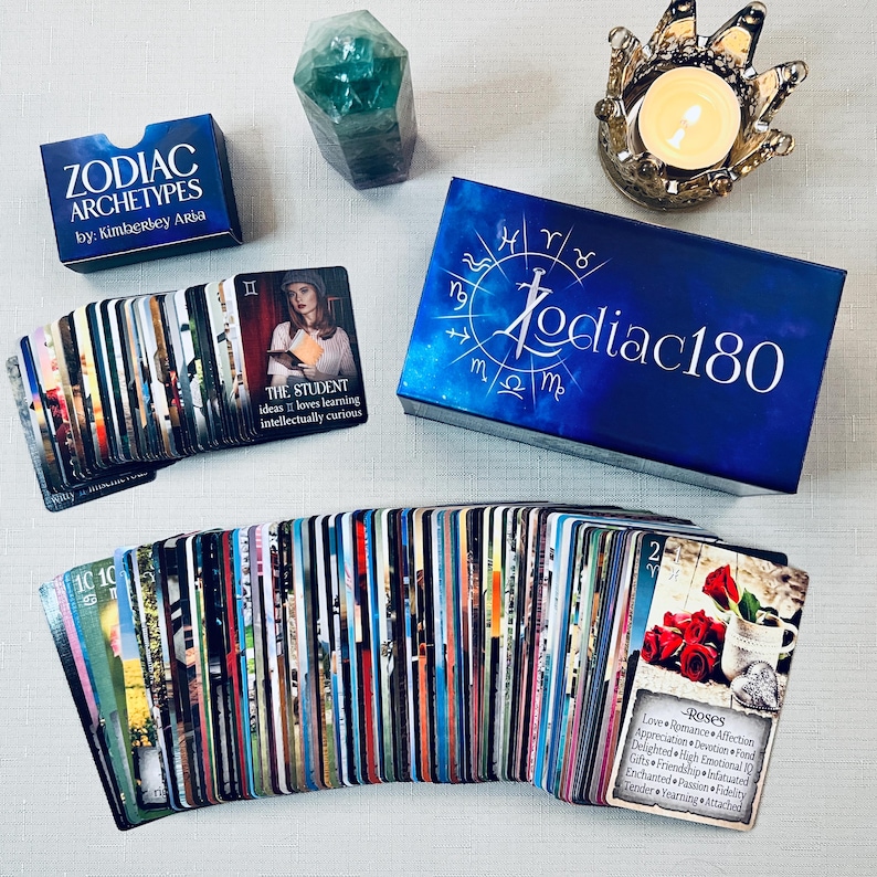 May include: A blue box with the text "Zodiac180" on it, a deck of cards with images of zodiac signs, and a green crystal. The cards have the text "The Student" and "Roses" on them.