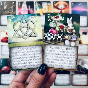 May include: Two tarot cards, one with a Celtic knot design and the words "Anam Cara" and the other with a white rabbit holding a pocket watch and the words "White Rabbit".