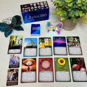 May include: A set of 10 Zodiac Archetype cards with colorful illustrations and text. The cards are laid out on a table with a butterfly and a box of cards in the background. The cards feature images of a yacht, a beehive, a shooting star, a white rabbit, a phoenix, a crown of thorns, a sunflower, and flamingos.