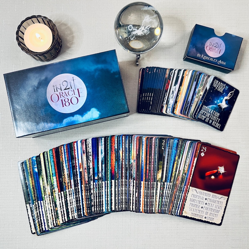 May include: A deck of 180 oracle cards with a blue box and a guidebook. The cards feature colorful images and text. The box has the text "IN21 ORACLE 180" on it. The guidebook has the text "IN21 ORACLE by KEDERLEY ARIA" on it.