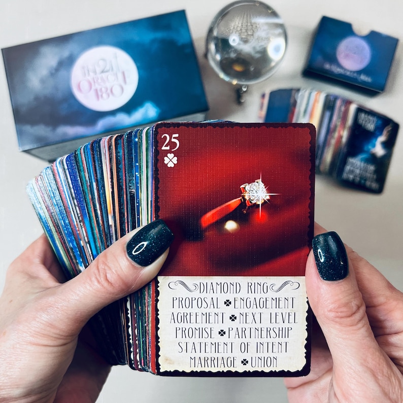May include: A red card with a diamond ring on a red velvet background. The card is from a deck of oracle cards and has the number 25 on it. The card also has the text "Diamond Ring, Proposal, Engagement, Agreement, Next Level, Promise, Partnership, Statement of Intent, Marriage, Union".