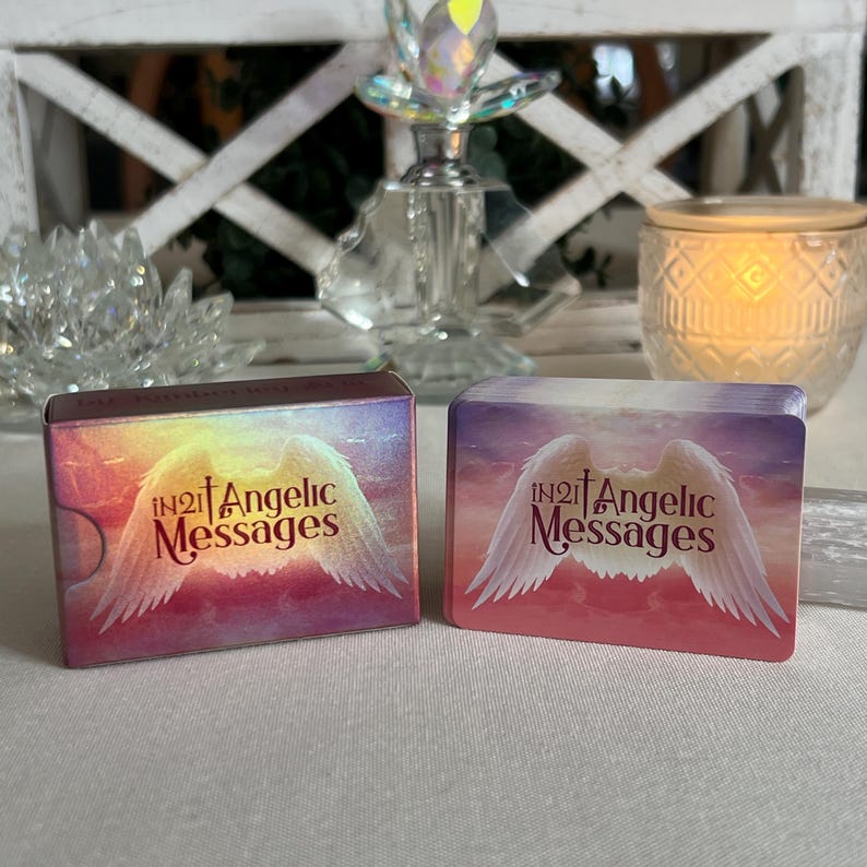 Puede incluir: Dos cajas de cartas de or&aacute;culo In2It Angelic Messages. Las cajas son rosas y moradas con un dise&ntilde;o de alas de &aacute;ngel blancas. El texto en las cajas es rojo y dice "In2It Angelic Messages".