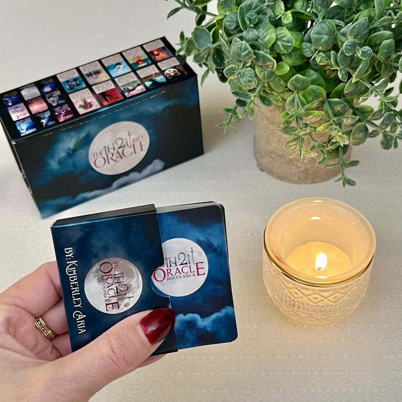 K&ouml;nnte beinhalten: Eine blaue und schwarze Schachtel mit dem Text "The In 21 Oracle" und "Bonus Deck" darauf. Die Schachtel ist ge&ouml;ffnet und eine kleinere blaue und schwarze Schachtel mit dem Text "The In 21 Oracle" ist sichtbar. Die kleinere Schachtel wird von einer Hand gehalten.