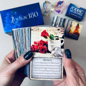 May include: A close-up of a card from a Zodiac Archetypes deck. The card features a red rose and a vintage-style teacup with a heart-shaped charm. The card's title is "Roses" and the text below lists associated keywords: Love, Romance, Affection, Appreciation, Devotion, Fond, Delighted, High Emotional IQ, Gifts, Friendship, Infatuated, Enchanted, Passion, Fidelity, Tender, Yearning, Attached.