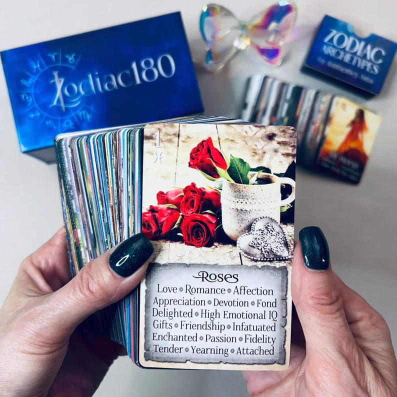 May include: A close-up of a card from a Zodiac Archetypes deck. The card features a red rose and a vintage-style teacup with a heart-shaped charm. The card's title is "Roses" and the text below lists associated keywords: Love, Romance, Affection, Appreciation, Devotion, Fond, Delighted, High Emotional IQ, Gifts, Friendship, Infatuated, Enchanted, Passion, Fidelity, Tender, Yearning, Attached.