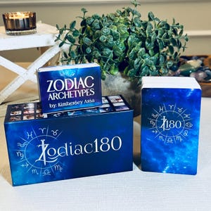 May include: A blue box with the text "Zodiac 180" and a circle of zodiac symbols. The box contains a deck of cards with a blue background and a circle of zodiac symbols with the text "Zodiac 180". The box also has a smaller box on top with the text "Zodiac Archetypes by: Kimberley Arba".