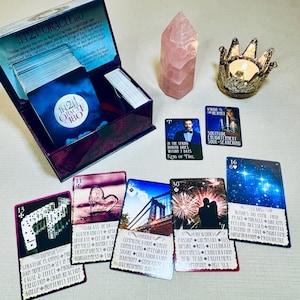 K&ouml;nnte beinhalten: Ein Tarot-Kartensatz mit einer violetten Schachtel, einem rosa Kristall und einem Kerzenhalter. Die Karten zeigen Bilder eines Herzens, einer Br&uuml;cke, eines Feuerwerks und von Sternen. Der Text auf den Karten lautet "In 21 Oracle 180", "Glas Herz", "Br&uuml;cke", "Feuerwerk" und "Sterne".