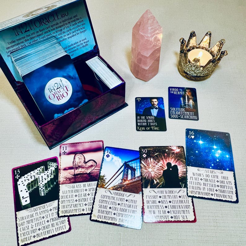 K&ouml;nnte beinhalten: Ein Tarot-Kartensatz mit einer violetten Schachtel, einem rosa Kristall und einem Kerzenhalter. Die Karten zeigen Bilder eines Herzens, einer Br&uuml;cke, eines Feuerwerks und von Sternen. Der Text auf den Karten lautet "In 21 Oracle 180", "Glas Herz", "Br&uuml;cke", "Feuerwerk" und "Sterne".