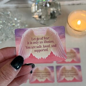 Puede incluir: Una tarjeta rosa y blanca con un par de alas de &aacute;ngel y el texto "Deja ir el miedo; es solo una ilusi&oacute;n. Est&aacute;s a salvo, amado y apoyado."
