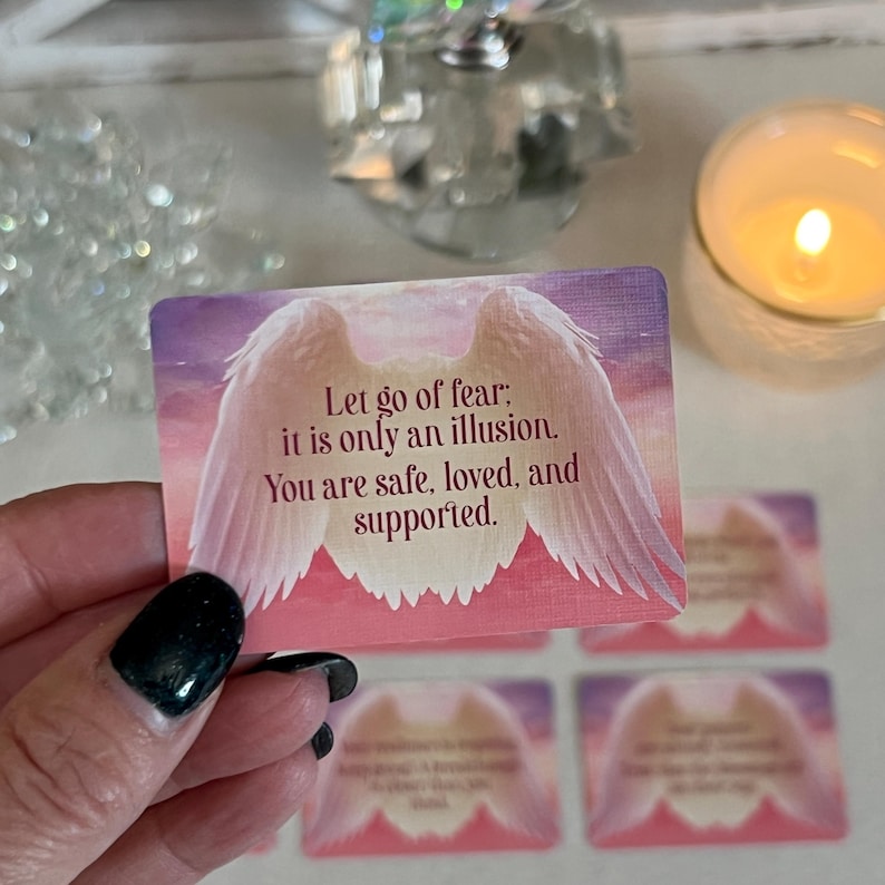 Puede incluir: Una tarjeta rosa y blanca con un par de alas de &aacute;ngel y el texto "Deja ir el miedo; es solo una ilusi&oacute;n. Est&aacute;s a salvo, amado y apoyado."