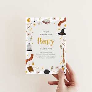 May include: A white invitation card with a gold border and a whimsical illustration of a wizard's hat, a cage, a wand, and other magical objects. The text on the card reads "Calling all Wizards and Witches Henry is turning seven The Wizard's Home Saturday October 10th 2 PM 123 Magical Alley, Las Vegas, NV RSVP to Luna at 123.456.7890".