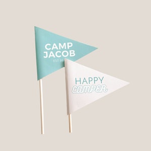 May include: Two triangular flags on wooden sticks. The blue flag says "Camp Jacob Est 20." The white flag says "Happy Camper" in teal.