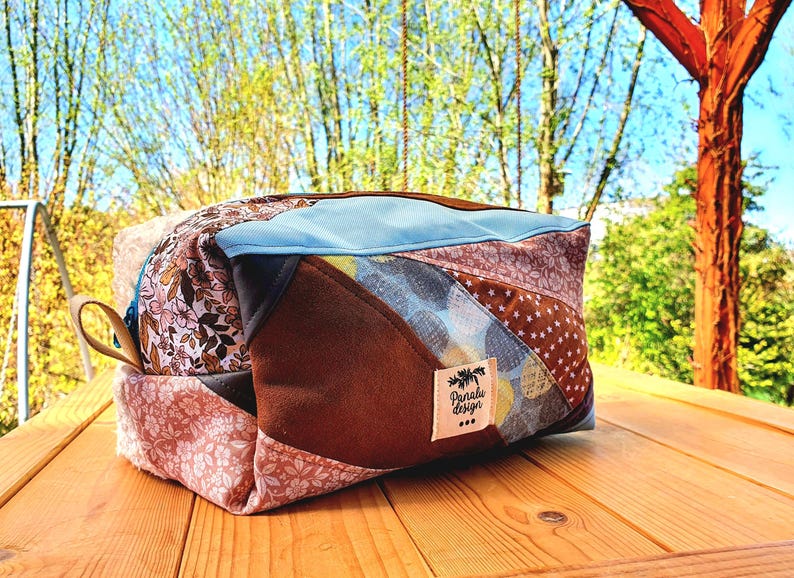 May include: A patchwork travel bag in shades of brown, pink, blue, and tan. The bag features various patterned fabrics, a light blue top, a brown handle, and a label reading "Paralu design".