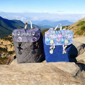 Può includere: Due zaini trapuntati con motivi diversi. Lo zaino a sinistra ha un tessuto trapuntato blu scuro e grigio con un motivo floreale sul lembo. Lo zaino a destra ha un tessuto trapuntato blu scuro con un motivo floreale sul lembo.