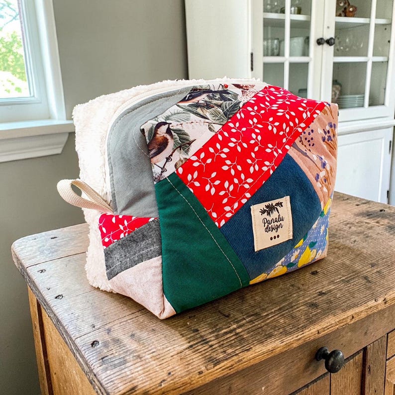 May include: A patchwork bag with a white, fluffy exterior and panels of colourful patterned fabric. The bag features red, green, blue, and floral print fabrics. A small tag reads "Panalu Design".