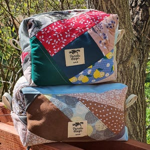 May include: Two patchwork fabric bags with cream handles. The top bag features red floral, green, and blue lemon-patterned fabric. The bottom bag has brown, tan, and blue fabrics. Each bag has a label that reads "Panalu Design".