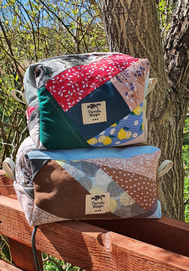 May include: Two patchwork fabric bags with cream handles. The top bag features red floral, green, and blue lemon-patterned fabric. The bottom bag has brown, tan, and blue fabrics. Each bag has a label that reads "Panalu Design".