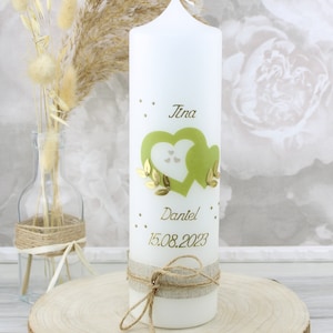 Könnte beinhalten: Weiße Kerze mit grünem Herzdesign und goldenen Akzenten. Die Kerze ist mit einem Juteband und einer Schnur verziert. Die Kerze ist personalisiert mit den Namen "Tina" und "Daniel" und dem Datum "15.08.2023".