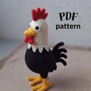 Könnte beinhalten: Ein handgehäkelter Hahn mit weißem Kopf, schwarzem Körper und gelben Füßen. Der Hahn hat einen roten Kamm und Kehllappen sowie einen gelben Schnabel. Der Text "PDF pattern" ist sichtbar.