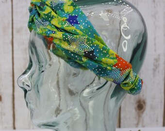 May include: A green, blue, and yellow patterned headband with silver glitter stars. The headband is on a glass mannequin head.