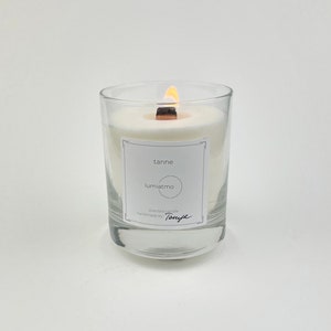 Könnte beinhalten: Eine brennende Duftkerze in einem klaren Glas. Die Kerze hat einen Holzdocht und ein weißes Etikett mit den Worten "tanne" und "lumiatmo". Die Kerze ist handgefertigt von Tonya.