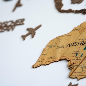 May include: Wooden world map with the continent of Australia prominently displayed. The map is made of light brown wood with engraved details, including country names and roads. A small wooden airplane and the word "Adventure" are also visible.