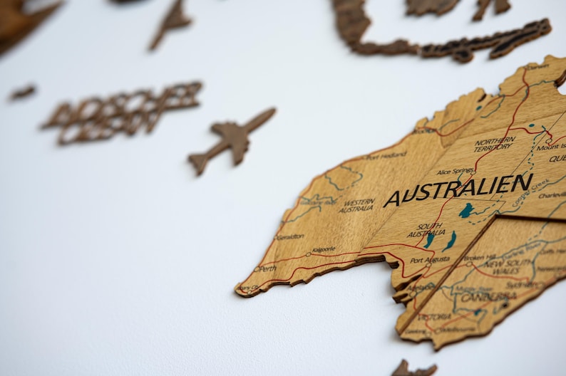 May include: Wooden world map with the continent of Australia prominently displayed. The map is made of light brown wood with engraved details, including country names and roads. A small wooden airplane and the word "Adventure" are also visible.