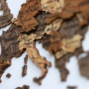 May include: A detailed wooden map of Europe, featuring countries like France, Germany, and Spain. The map is intricately carved with city names and borders, showcasing a vintage aesthetic. The color palette includes shades of brown and beige.
