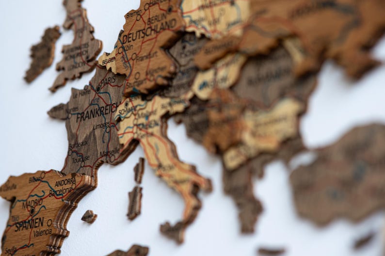 May include: A detailed wooden map of Europe, featuring countries like France, Germany, and Spain. The map is intricately carved with city names and borders, showcasing a vintage aesthetic. The color palette includes shades of brown and beige.