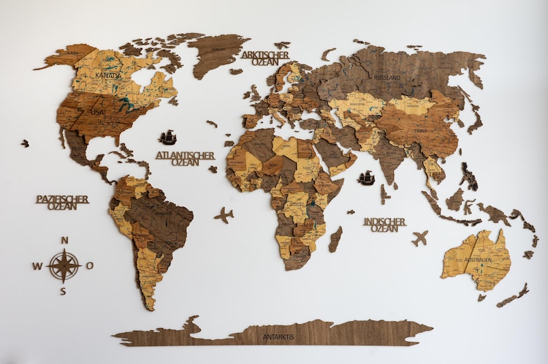 May include: A wooden world map with detailed country outlines, in shades of brown and tan, mounted on a white background. Includes compass rose, ships, and airplane cutouts. Text labels oceans and continents.