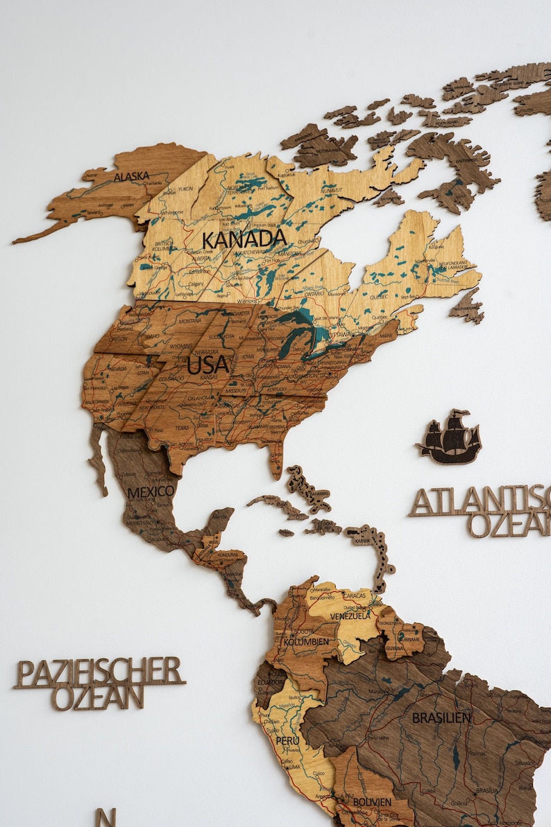 May include: A wooden world map with detailed country outlines and labels, including "KANADA", "USA", and "MEXICO". The map features varying shades of brown and tan, with text labels in a serif font. A ship silhouette is also present.