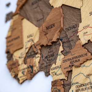 May include: A detailed wooden map of Africa, featuring countries like Nigeria, Niger, and Chad. The map is crafted from various shades of brown wood, with country names and geographical details etched into the surface. The map is mounted on a white background.