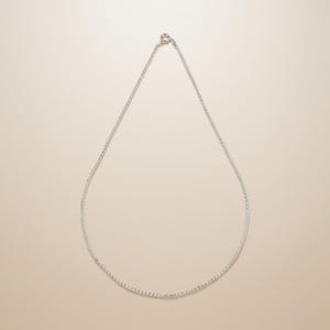 May include: A delicate silver necklace with a fine chain. The necklace is displayed against a neutral background, highlighting its simple elegance. The chain is connected with a small clasp.