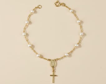 May include: A gold chain bracelet featuring small white pearls spaced along the links. The bracelet includes a central oval medal depicting a figure and a dangling gold cross pendant, secured with a circular spring ring clasp closure.