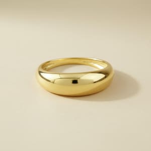 May include: A gold-colored ring with a smooth, rounded design. The ring has a polished, reflective surface, catching the light. The ring is a simple band, suitable for everyday wear. The ring is likely made of gold or a gold-colored metal.