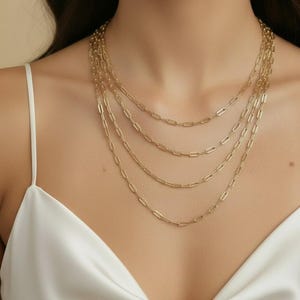 May include: A layered gold-toned necklace set. The necklaces feature a delicate paperclip chain design. The chains are of varying lengths, creating a cascading effect. The jewelry is displayed against a neutral background, highlighting the warm metallic tones.