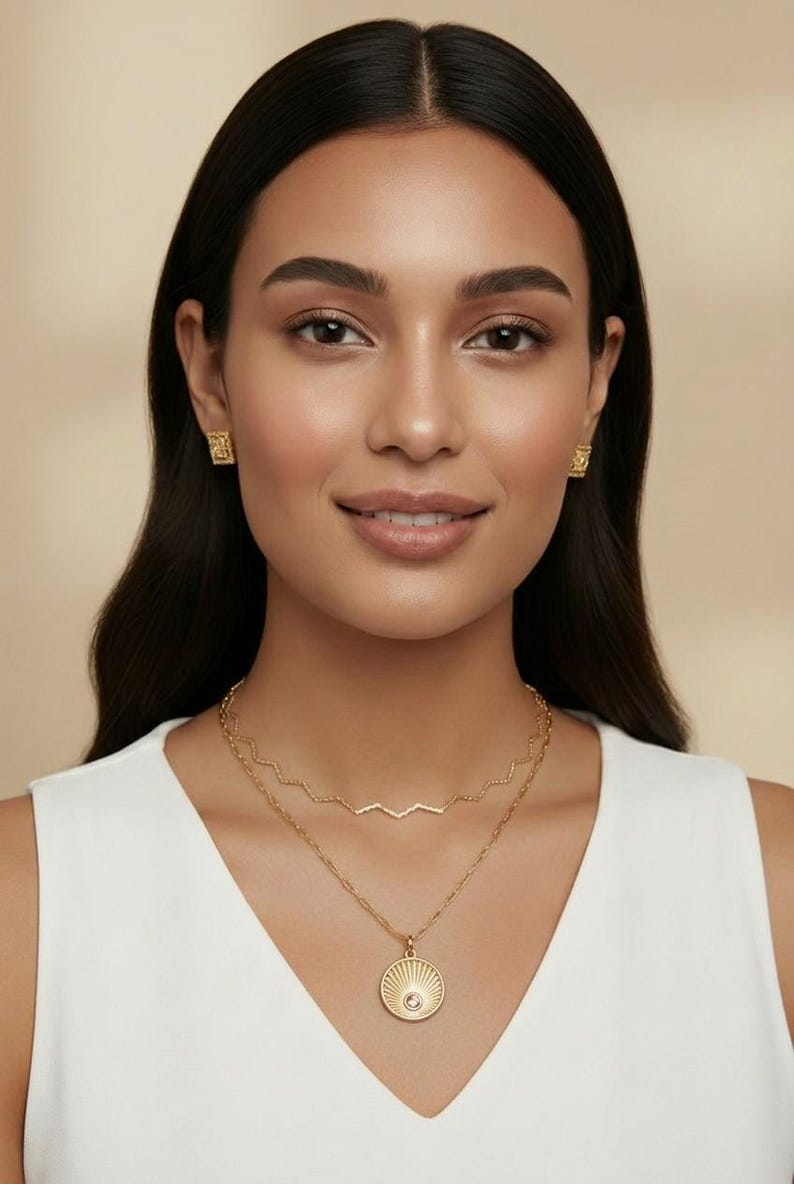 May include: A gold jewelry set consisting of a pair of small square stud earrings and a two-layer necklace. The top layer is a thin zigzag chain, while the bottom layer features a round pendant with a sunburst design and a central stone.
