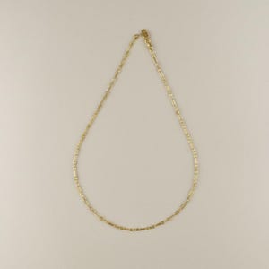 May include: A delicate gold necklace with a repeating rectangular link design. The necklace is displayed on a neutral background, showcasing its simple elegance. The chain is secured with a small clasp.