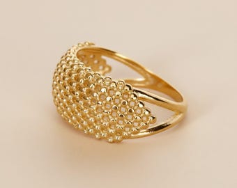 May include: A gold-colored ring with a textured, beaded design across the top. The ring has a split band and a rounded shape, creating a unique and elegant look. The ring is likely made of gold or a gold-toned metal.