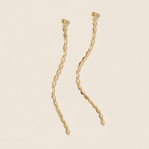 May include: A pair of long gold earrings featuring a small spherical stud at the top connected to a delicate, wavy chain composed of small, flat, oval-shaped metallic links that hang vertically in a graceful, elongated, and fluid design.